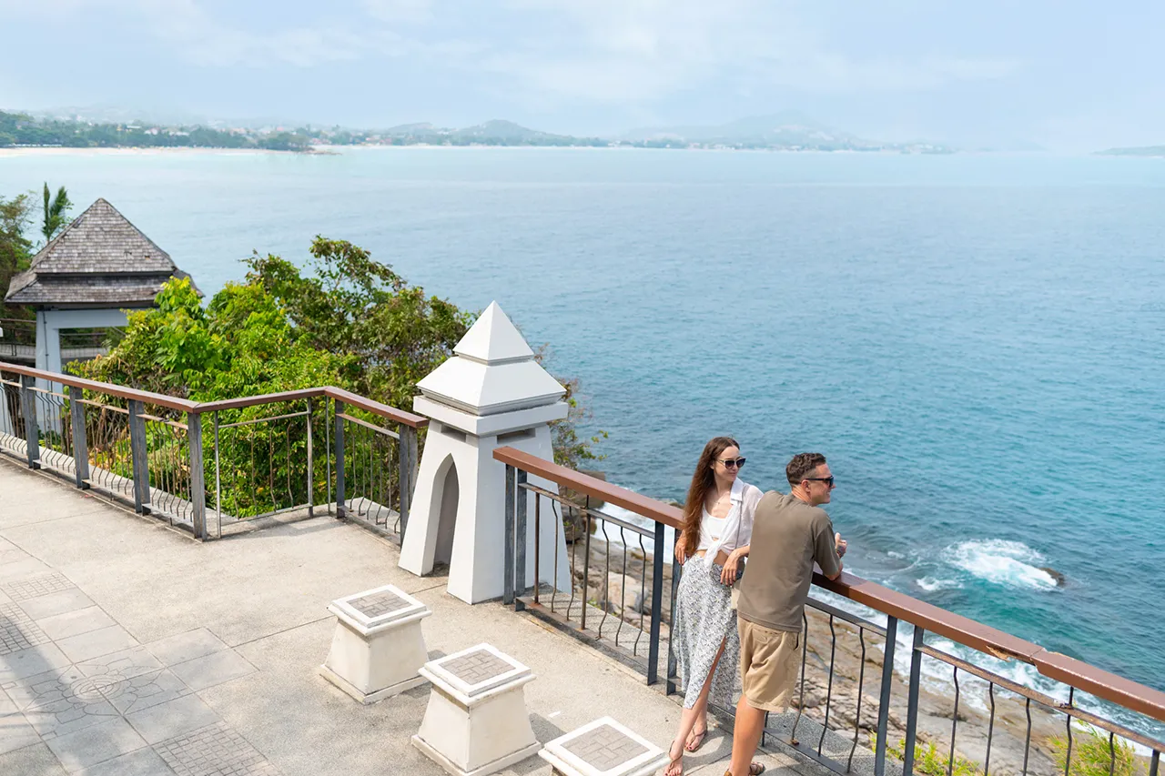 A couple enjoying the breathtaking view at Lat Ko Viewpoint, overlooking the expansive ocean and lush green cliffs of Koh Samui.