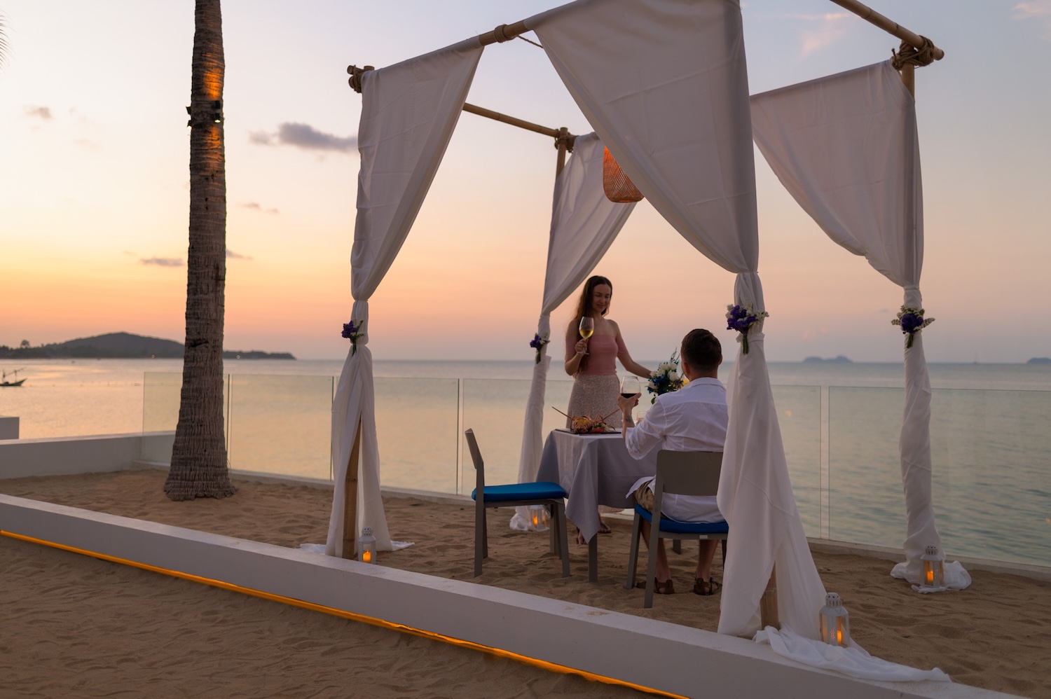 Romantic beachfront dinner for a couple on a private beach at Explorar Koh Samui, with candlelit table and ocean waves in the background.