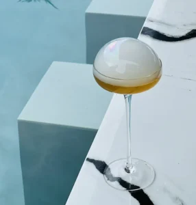 A beautifully crafted Summertime in Samui cocktail with a smoke bubble garnish, set against the luxury beachfront of Explorar Koh Samui.